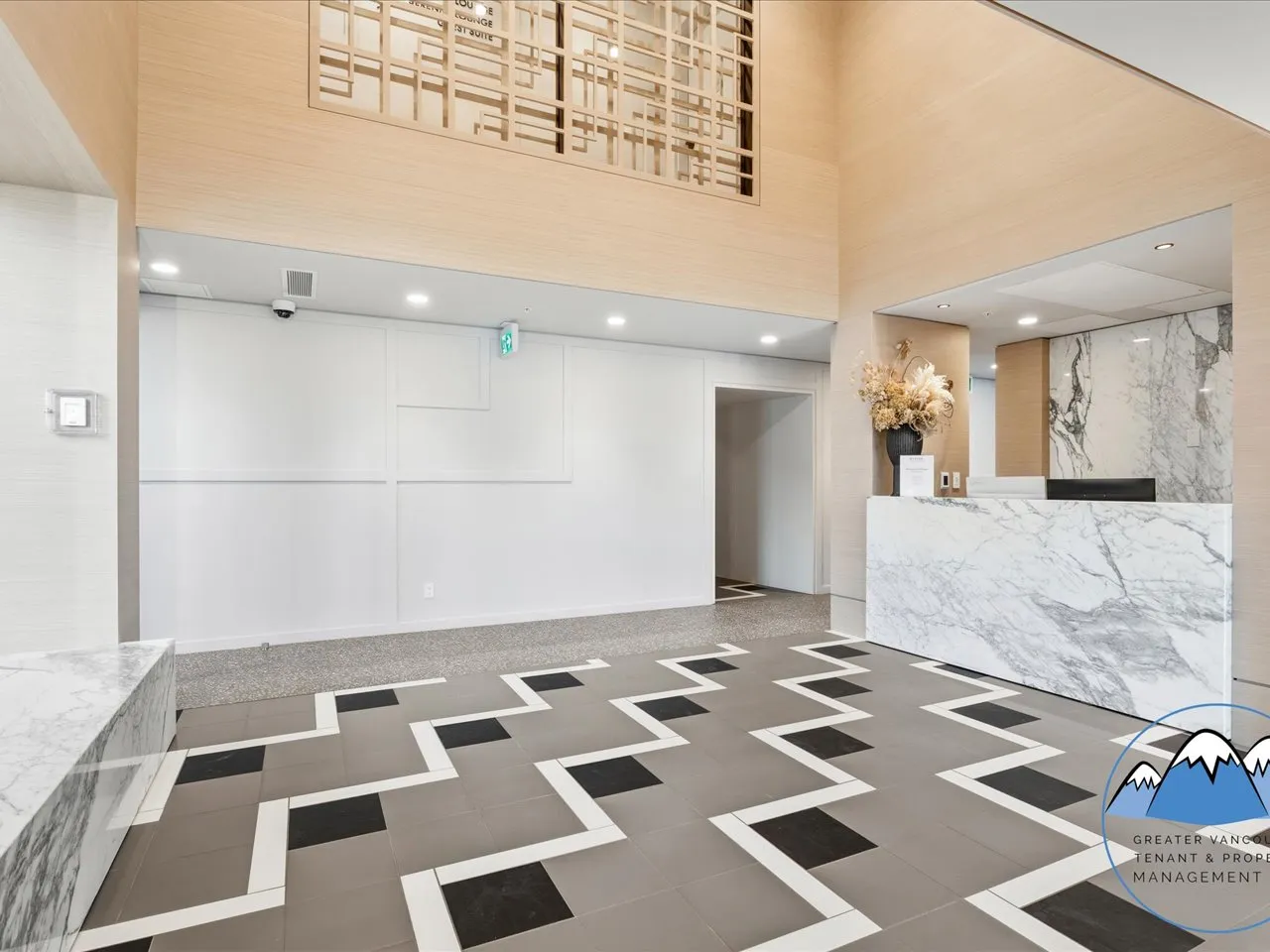 Double-height lobby with a marble reception desk, patterned tile floor and warm wood ceiling.