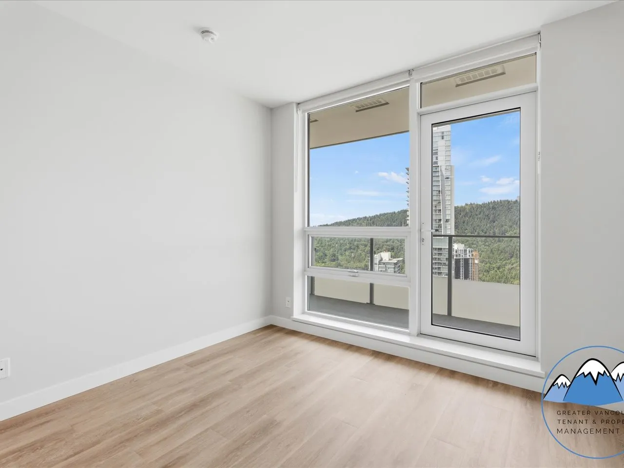 Bedroom with corner windows overlooking greenery and neighbouring towers.