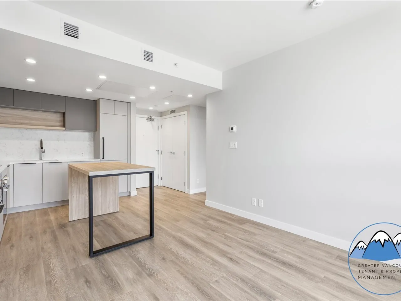 Living and dining area with the kitchen at one side, a large blank feature wall and the suite entry.
