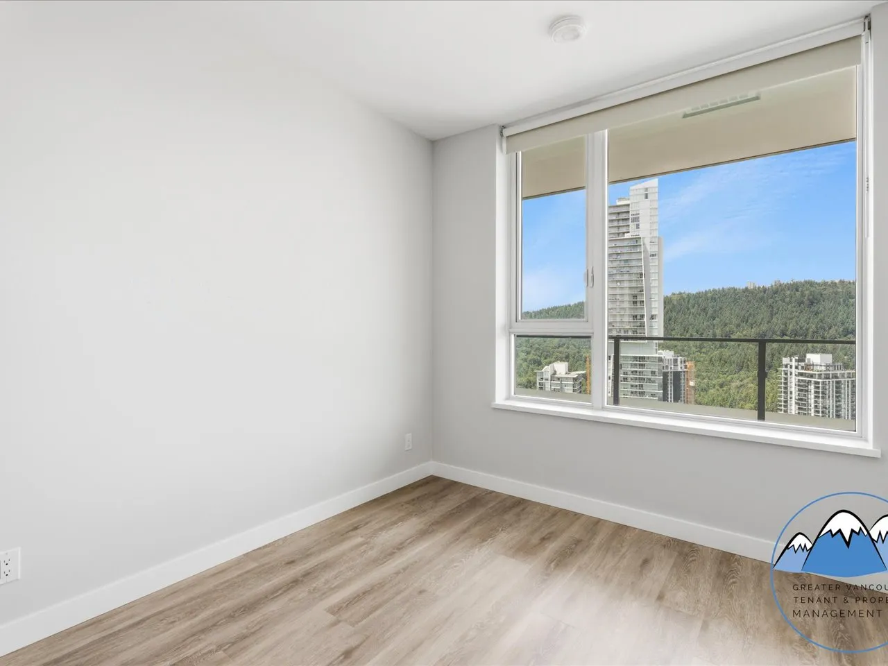 Bright room with a large window framing forested hillsides and the Burquitlam skyline.