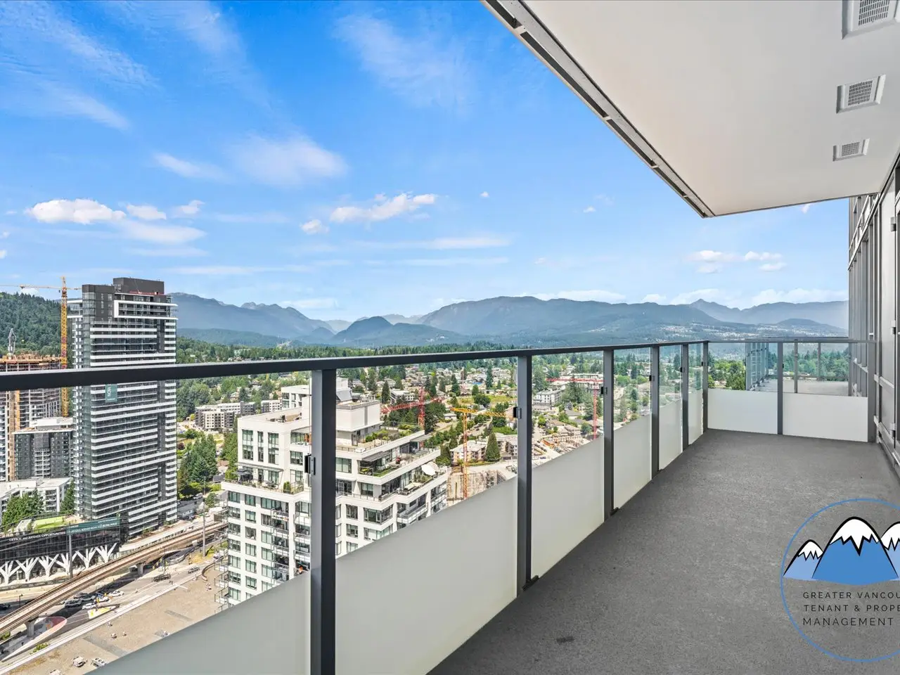 Balcony view across Burquitlam towers and the SkyTrain guideway toward the North Shore mountains.