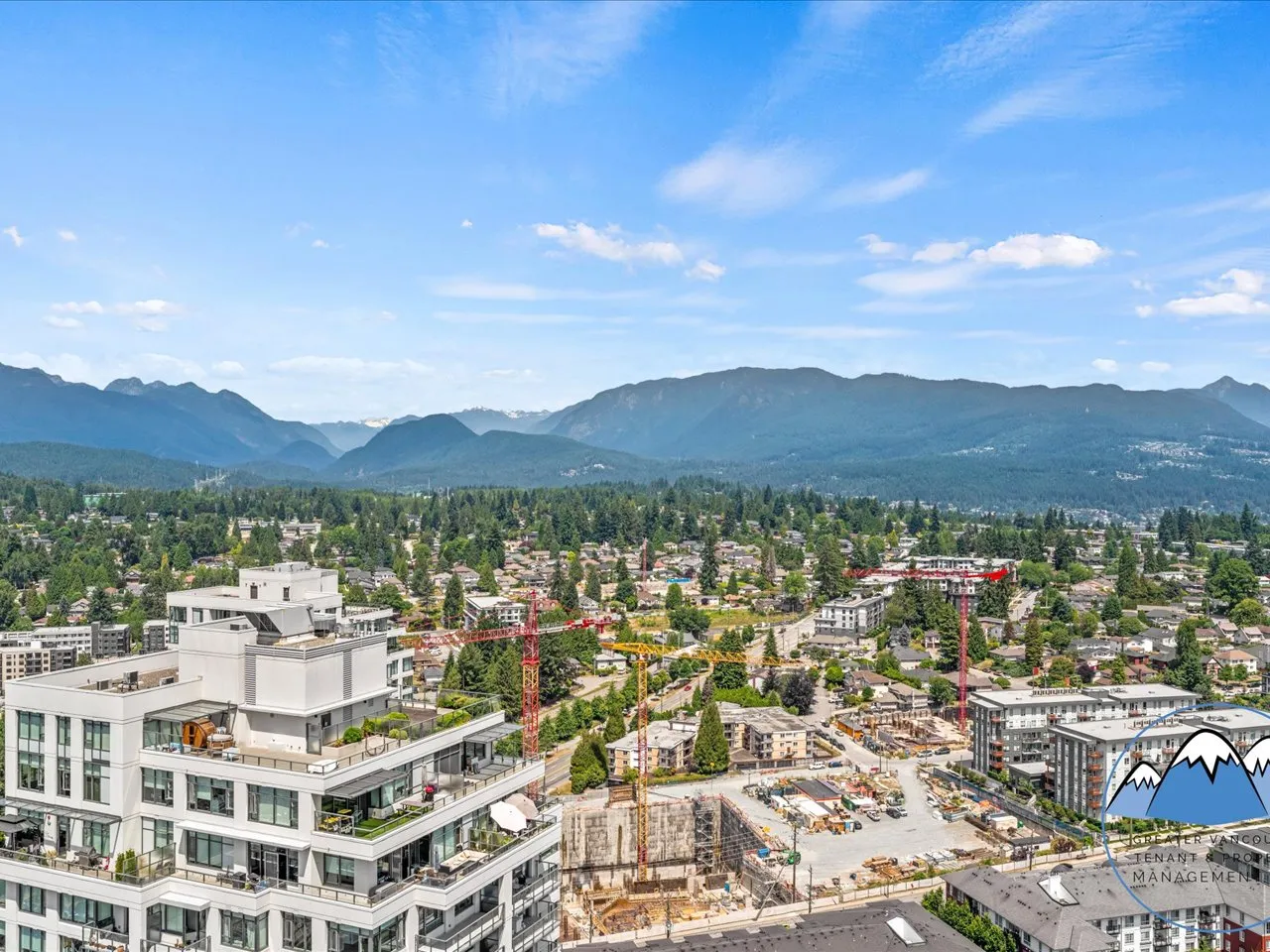 Elevated view across Coquitlam rooftops and treetops to the layered coastal mountain range.