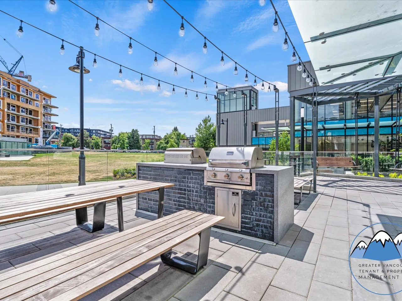 Outdoor lounge with built-in barbecues, communal timber tables and string lighting.